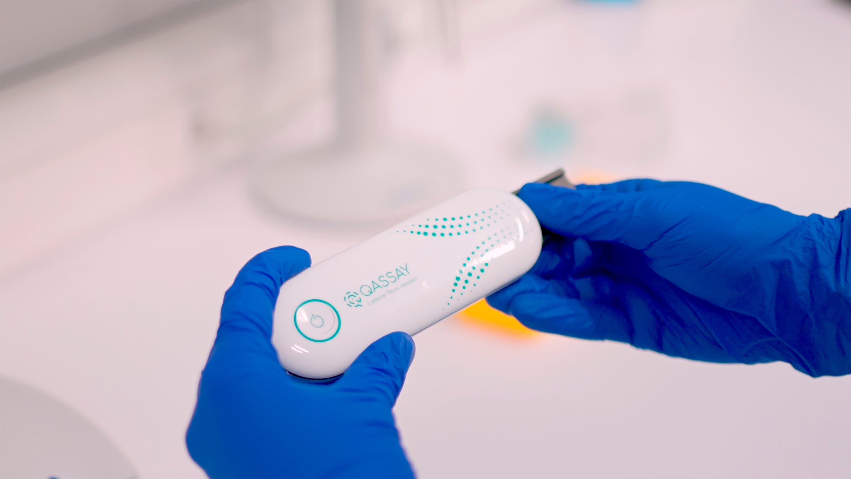 A person holding a Qassay medical testing device in a laboratory setting.